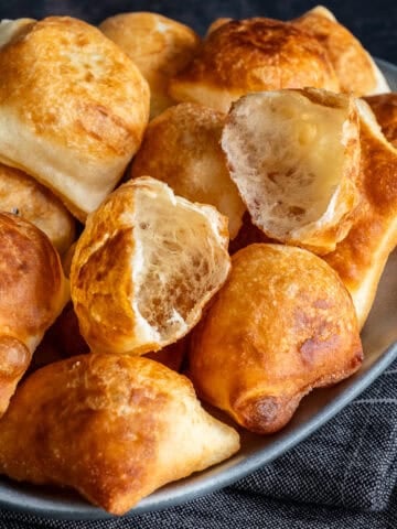 Close-up of golden, puffy Turkish pişi, with two torn open to show their light and airy inside.