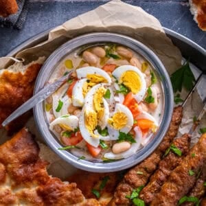 Overhead view of Antalya piyazi topped with hard-boiled eggs, tomatoes, onions and parsley, served with grilled şiş köfte and Turkish bread.