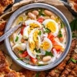 Overhead view of Antalya piyazi (Turkish white bean salad with tahini sauce), topped with hard-boiled eggs, tomatoes, onions and parsley, served with grilled şiş köfte and Turkish bread.
