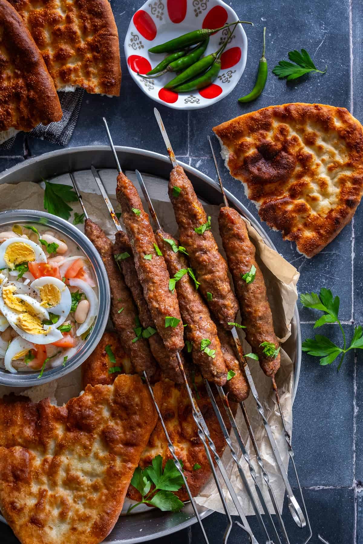 Turkish tirnak pide served with grilled shish kofte skewers and Antalya piyazi, with fresh green peppers and parsley.